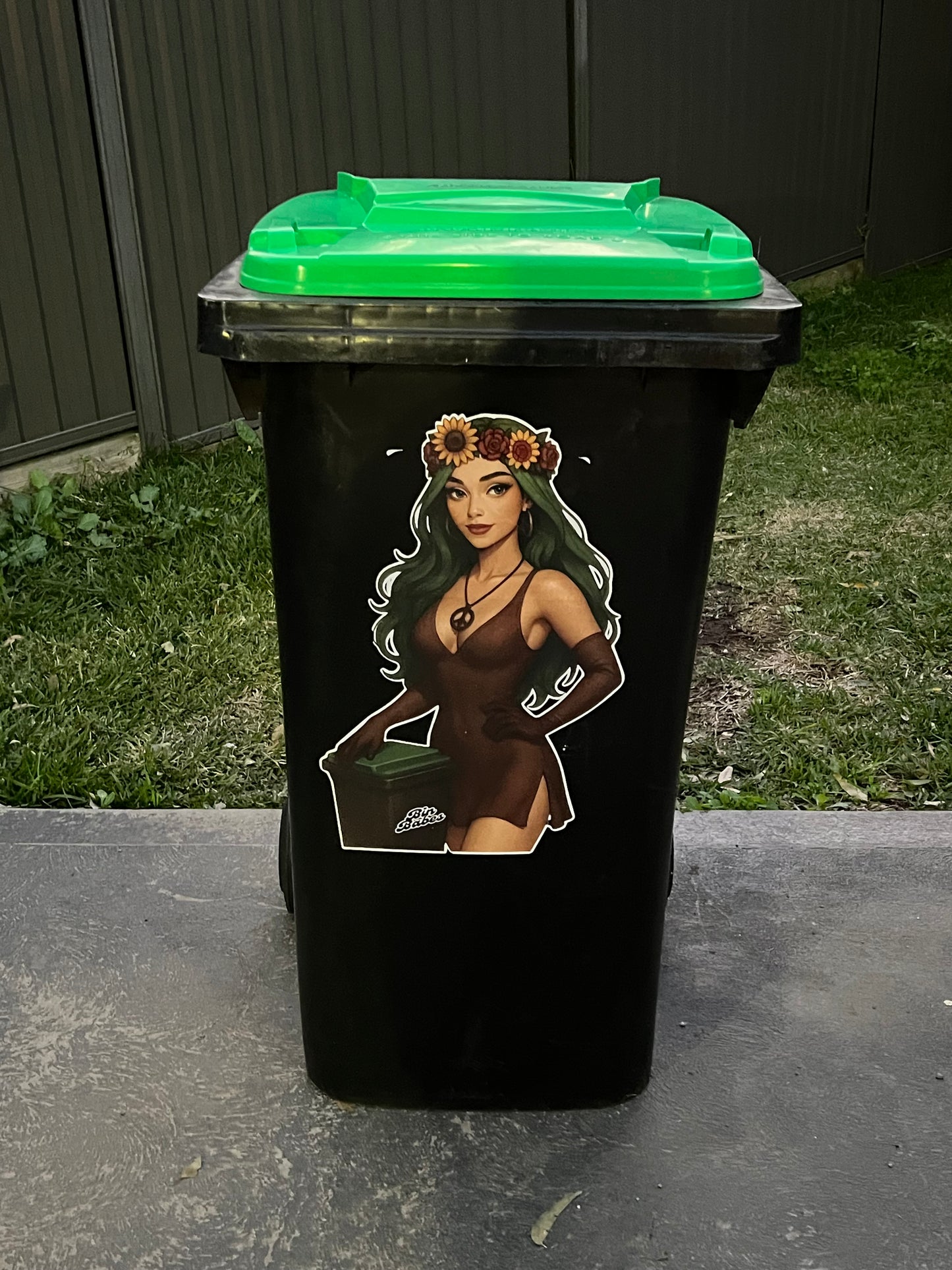 Black trash bin with a graphic design of a person with flowers on their head outdoors.