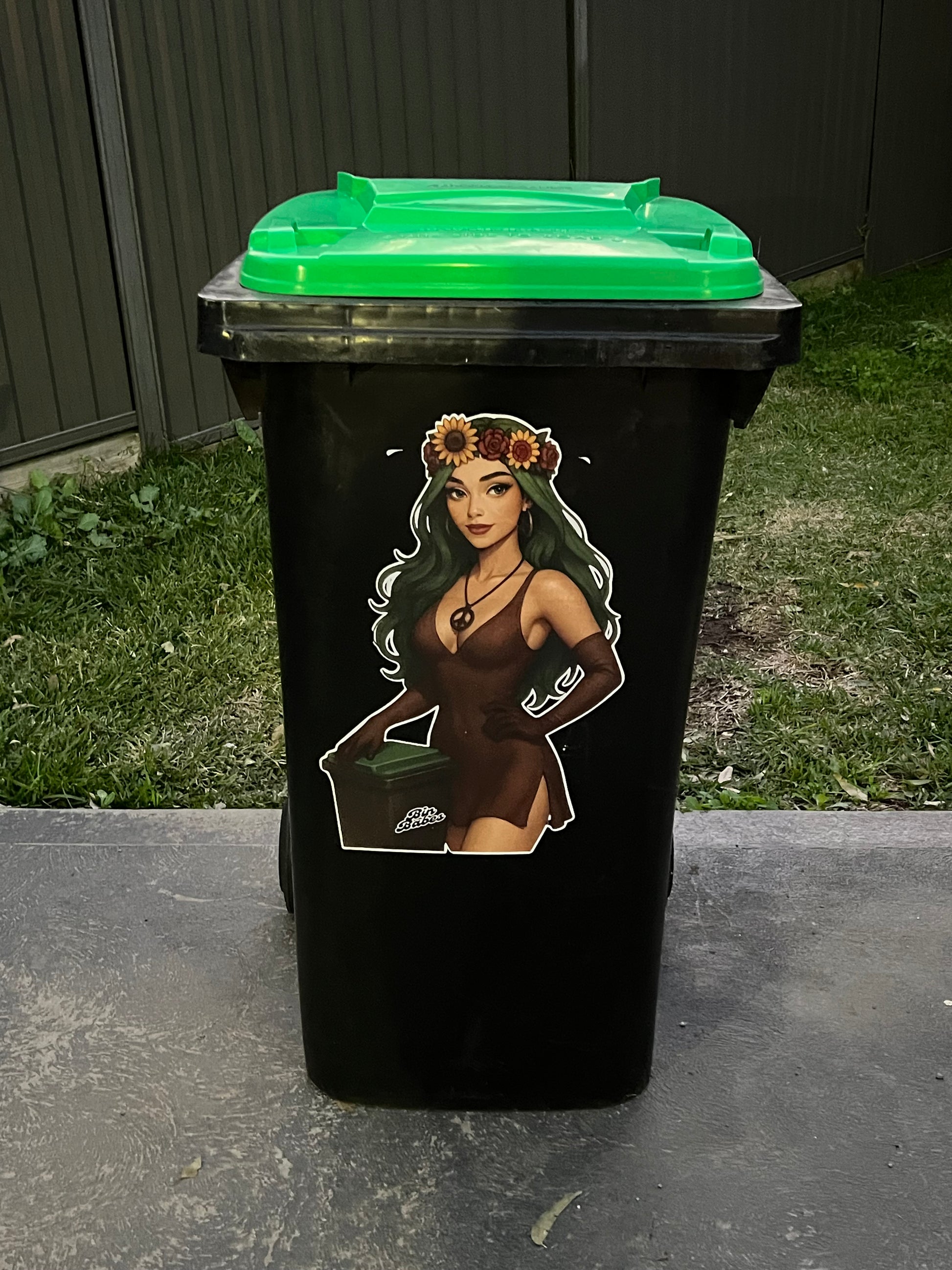 Black trash bin with a graphic design of a person with flowers on their head outdoors.